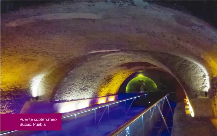 Interior del Puente subterráneo Bubas, en Puebla: túnel de piedra con pasillo iluminado en azul y luces amarillas y blancas sobre los arcos.