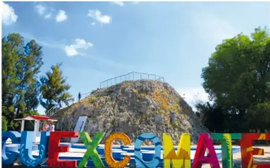 Letras de colores que forman la palabra CUEXCOMATE al pie del géiser, con árboles y un pequeño quiosco.