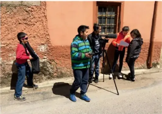 Niño frente a una cámara de video en un salón, con otro niño de espaldas.