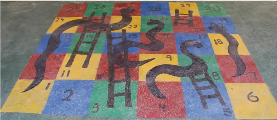 Tablero de serpientes y escaleras pintado en el piso con números del 1 al 30, escaleras de madera y serpientes dibujadas.