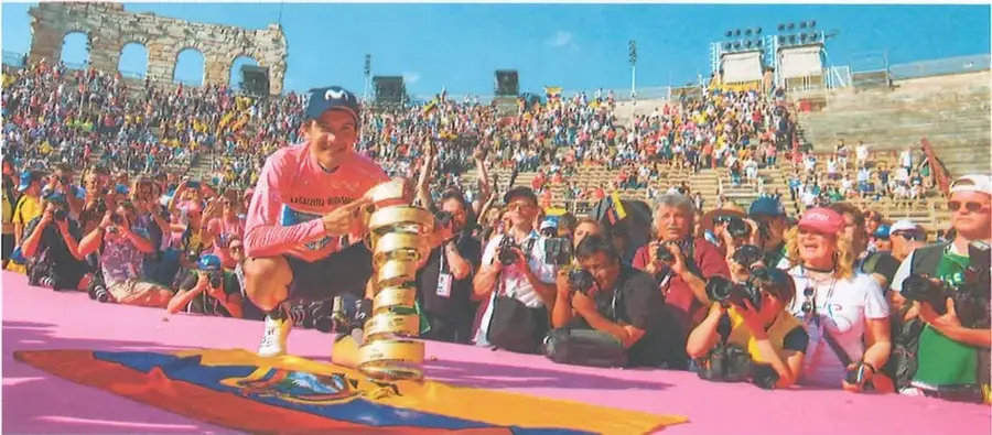 Richard Carapaz sostiene el trofeo del Giro de Italia frente a una multitud, en un ambiente de celebración.