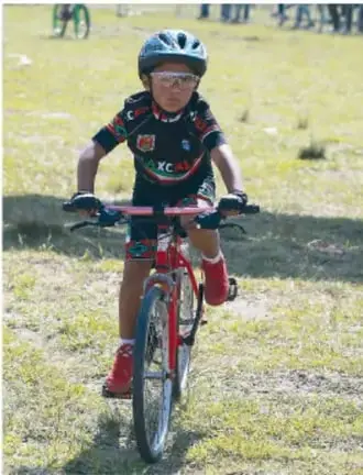 Fotografía de un niño con casco y uniforme deportivo montando una bicicleta roja en un parque, como ejemplo de actividad física.