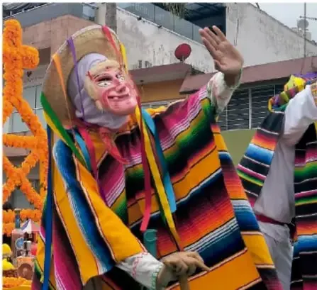 Persona disfrazada con vestimenta tradicional mexicana de colores y máscara, alusiva a las Catrinas o tradiciones del Día de Muertos.
