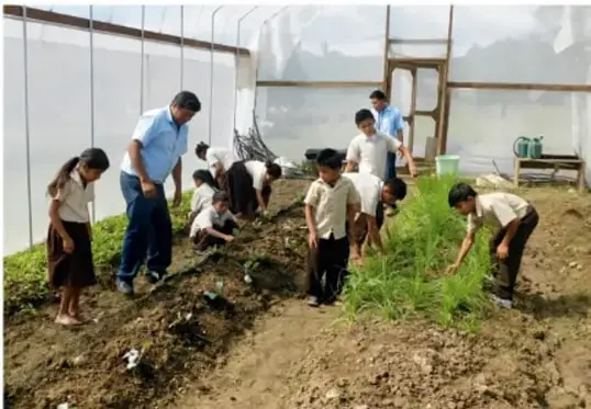 Niños y niñas trabajando en un invernadero o huerto escolar, sembrando y cuidando plantas junto a un adulto.