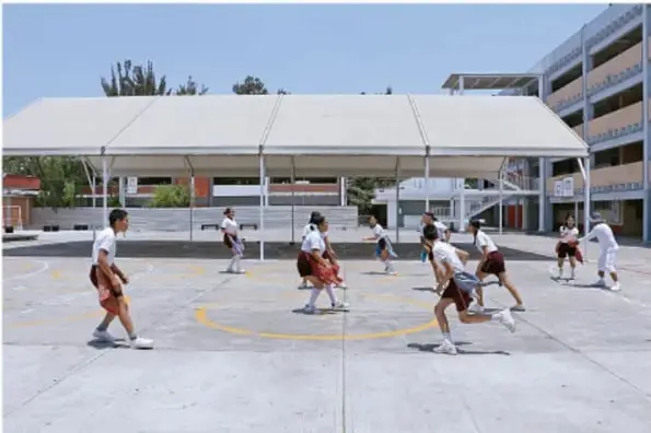 Grupo de estudiantes de secundaria jugando basquetbol en la cancha techada de su escuela.