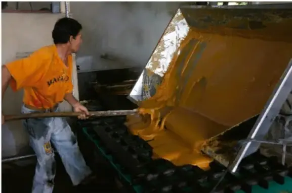 Trabajador en planta industrial vertiendo material dorado en un molde, ilustrando innovación de proceso