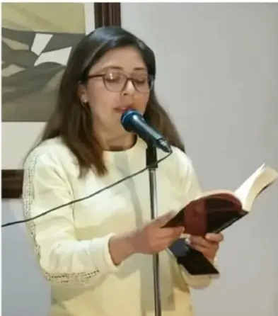 Fotografía de una joven leyendo un libro frente a un micrófono en un evento de lectura en voz alta.