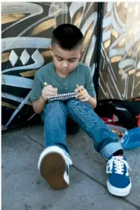 Niño sentado en el suelo manipulando un pequeño objeto, con un mural de fondo.