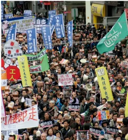 Multitud de personas en una protesta con carteles y banderas, principalmente en chino.