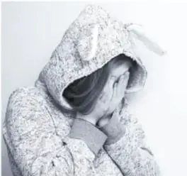 Fotografía en blanco y negro de una adolescente con capucha, sentada y con la cabeza apoyada en las manos, que ilustra los cambios emocionales.