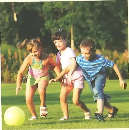 Tres niños juegan con una pelota en un espacio verde durante un día soleado.