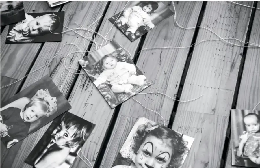 Fotografías en blanco y negro de bebés y niños pequeños extendidas sobre una mesa de madera gris, algunas sujetas con hilo, como álbum de recuerdos familiares antiguos.