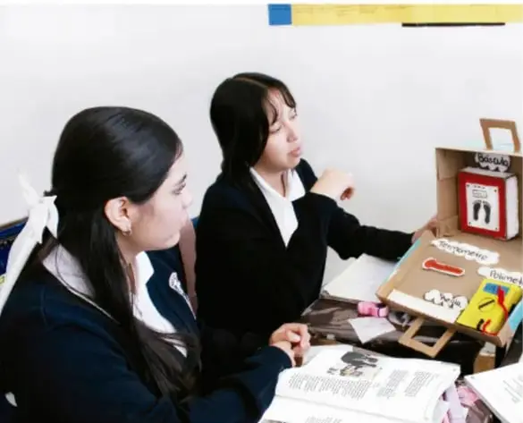 Fotografía de dos estudiantes trabajando con un maletín de instrumentos de medición y materiales sobre una mesa.