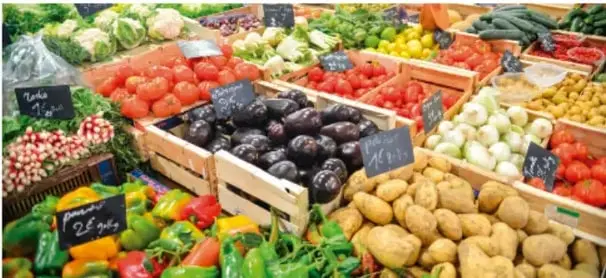Fotografía de un puesto de mercado con variedad de frutas y verduras en cajones de madera (jitomate, berenjena, papa, cebolla, chile), ilustrando los alimentos como fuente de sustancias que reaccionan en el organismo.