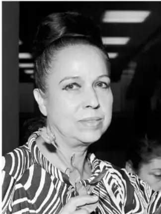 Retrato en blanco y negro de una mujer sonriente con peinado alto y blusa con estampado de rayas.