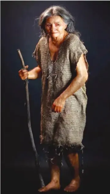 Reconstrucción escultórica a tamaño real de una mujer prehistórica de pie, con vestimenta tosca y bastón.