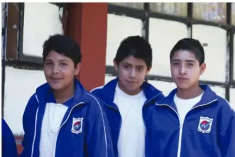 Tres estudiantes con uniforme escolar azul posando frente a la cámara.