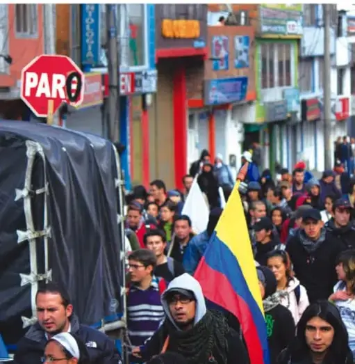 Marcha callejera con personas portando banderas de Colombia y un cartel de 'PARE'.