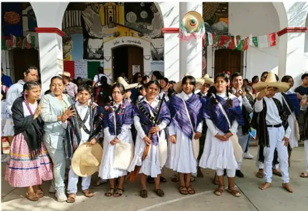 Fotografía de un grupo de estudiantes vestidos con trajes típicos en un patio escolar decorado con banderas, realizando una presentación cultural.