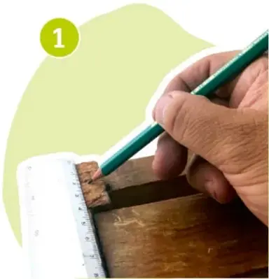 Manos de una persona midiendo con regla y marcando con lápiz verde una línea sobre la madera del huacal.