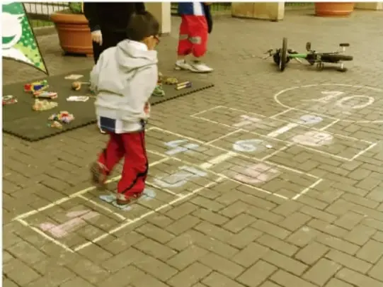 Niño saltando en un pie sobre las casillas del avión mientras otros observan.