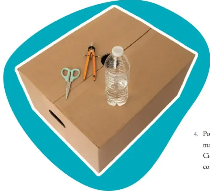 Fotografía de una caja de cartón abierta con una botella de plástico transparente, un compás, tijeras y una cinta métrica sobre ella.