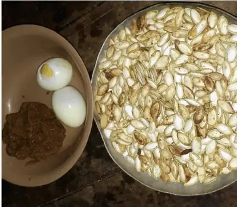 Fotografía de un recipiente con huevos sancochados (dos enteros y uno partido) junto a un plato lleno de semillas tostadas de calabaza, alimentos simbólicos usados en la ceremonia.