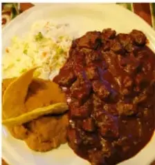 Plato con tacos o enchiladas bañadas en salsa, con lechuga, crema y queso.