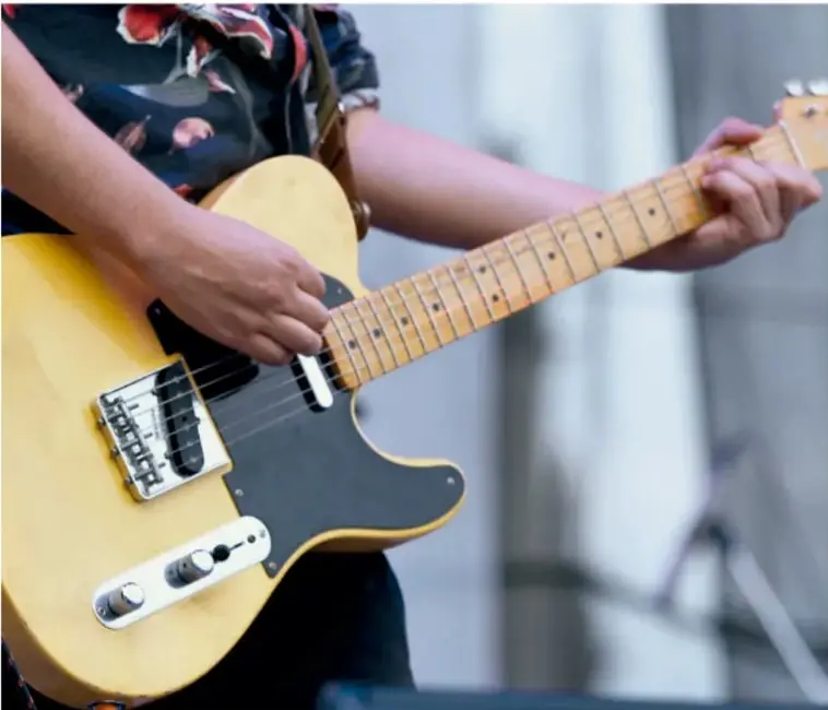 Fotografía de una persona tocando una guitarra eléctrica amarilla estilo Telecaster, probablemente como ejemplo de grupo social o interés que forma parte del microsistema o mesosistema del individuo.