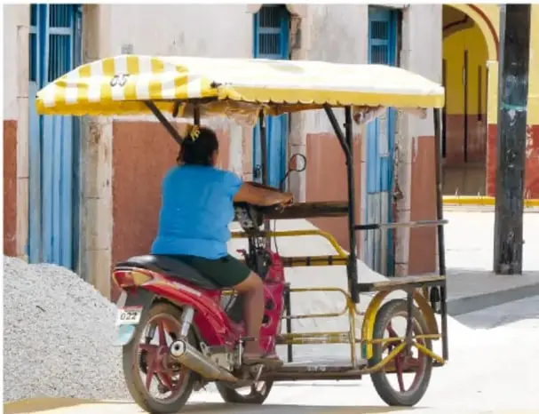 Persona conduciendo un mototaxi (moto con carrocería cubierta de toldo amarillo) por una calle de un pueblo mexicano (medio de transporte terrestre actual).