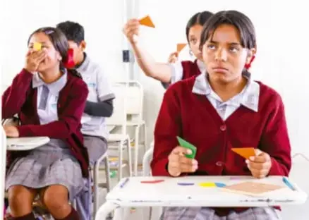 Fotografía de estudiantes en el aula que evalúan con tarjetas de colores (verde y naranja) un trabajo, uno de ellos muestra expresión de desaprobación.