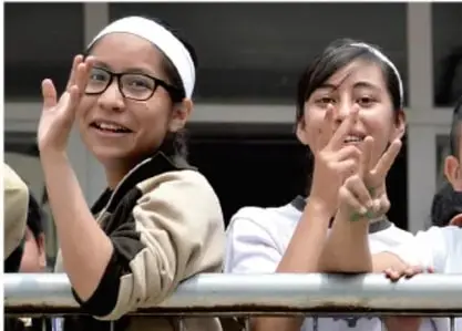 Fotografía de dos estudiantes mujeres de secundaria sonrientes saludando y haciendo el gesto de paz, con bandas en la cabeza.