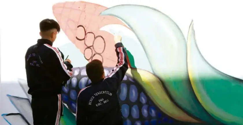 Fotografía de dos jóvenes de espaldas pintando una gran estructura artística colorida de formas curvas verde y rosa.