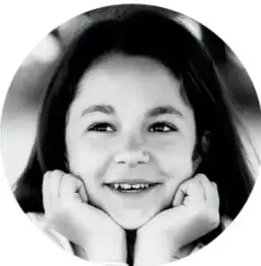 Fotografía en blanco y negro de una niña sonriente con las manos en el rostro, mirando a la cámara.