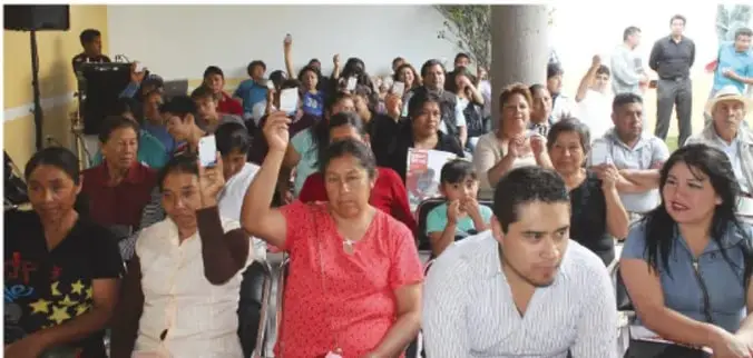 Fotografía de una asamblea o reunión ciudadana con personas sentadas y algunas levantando la mano, lo que ilustra la participación ciudadana.