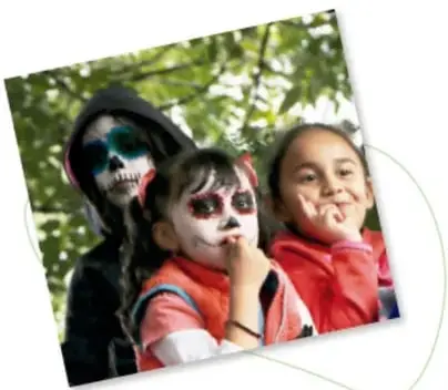 Niños con gorros de fiesta sentados en un mantel en el parque, con pastel y velas: fiesta de cumpleaños.