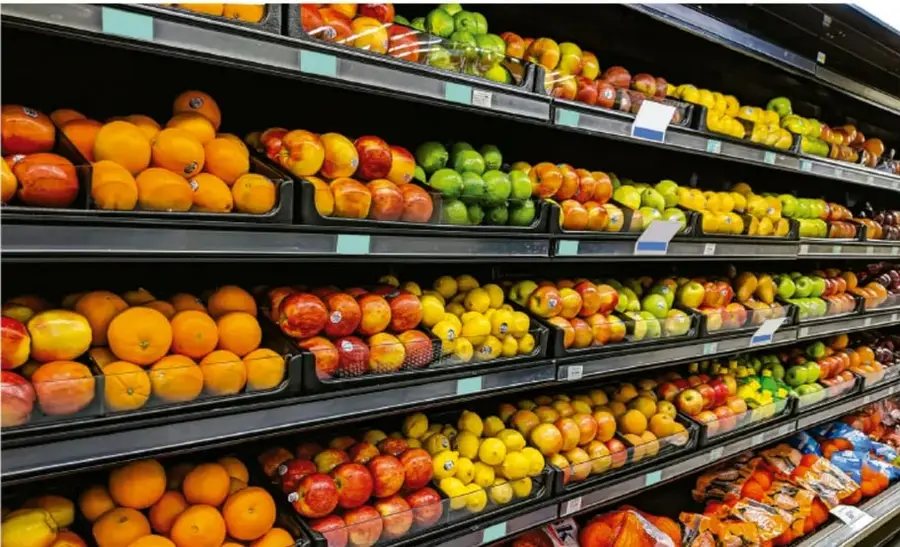 Estantería de supermercado con frutas y verduras frescas, como naranjas, manzanas, limones y jitomates.