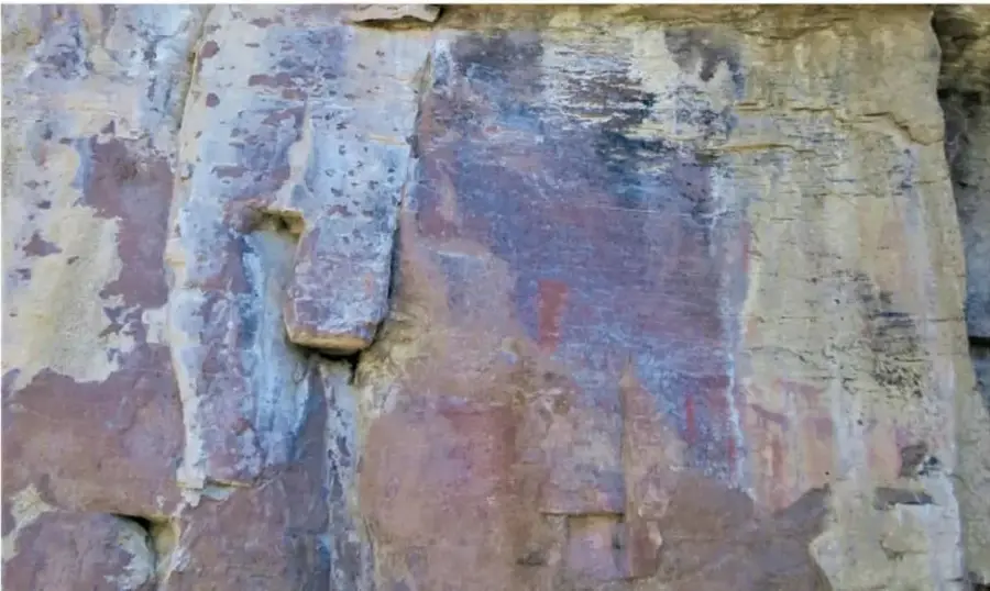 Fotografía de la pared rocosa de la cueva El Meco, con manchas y restos de pintura en tonos rojizos, grises y violáceos sobre la piedra.