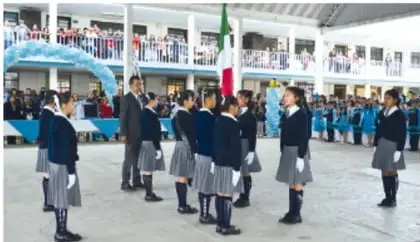 Foto de un patio escolar con alumnos en formación y una bandera mexicana.