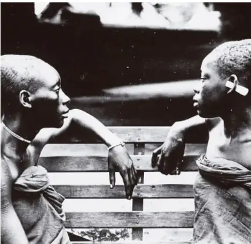 Fotografía en blanco y negro de dos niños africanos sentados en una banca, mirándose, como símbolo de la infancia afectada por la exclusión.