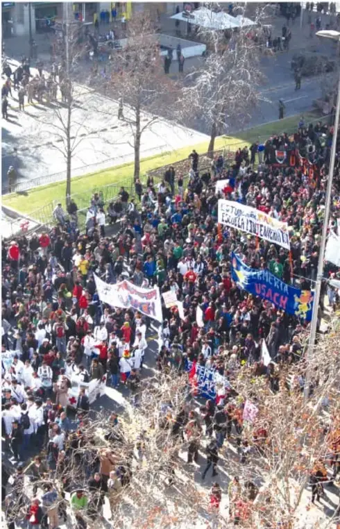 Multitud en una protesta callejera con pancartas y banderas, vista desde arriba.