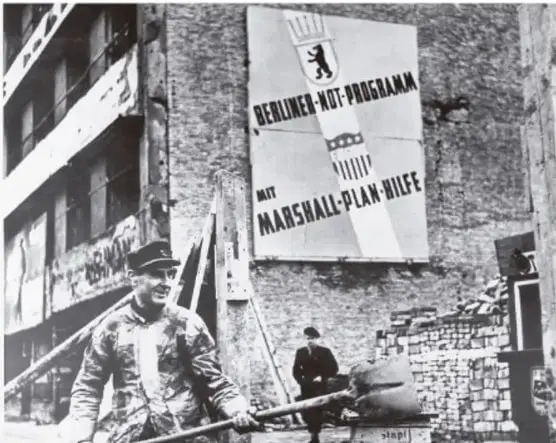 Fotografía histórica en blanco y negro de un edificio destruido en Berlín con un cartel que dice 'BERLINER NOT-PROGRAMM MIT MARSHALL-PLAN-HILFE', en referencia al Plan Marshall.