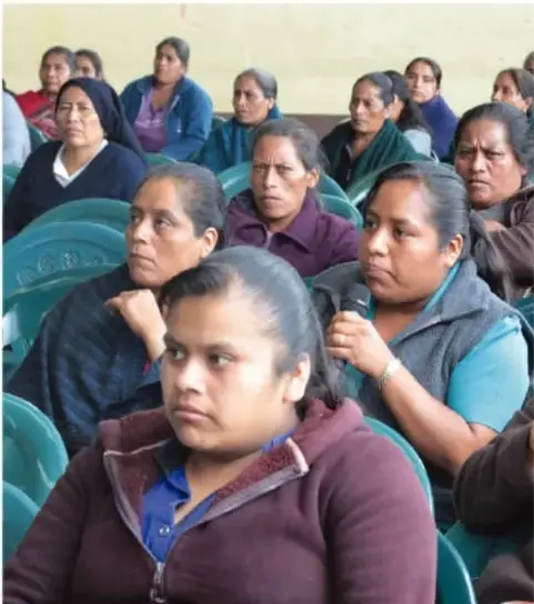 Fotografía de un grupo de mujeres sentadas en sillas, participando en una reunión o asamblea comunitaria.