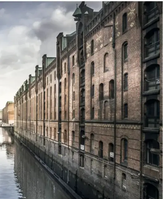 Edificio de ladrillo de varios pisos junto a un canal; sus ventanas se repiten con regularidad y se reflejan en el agua.