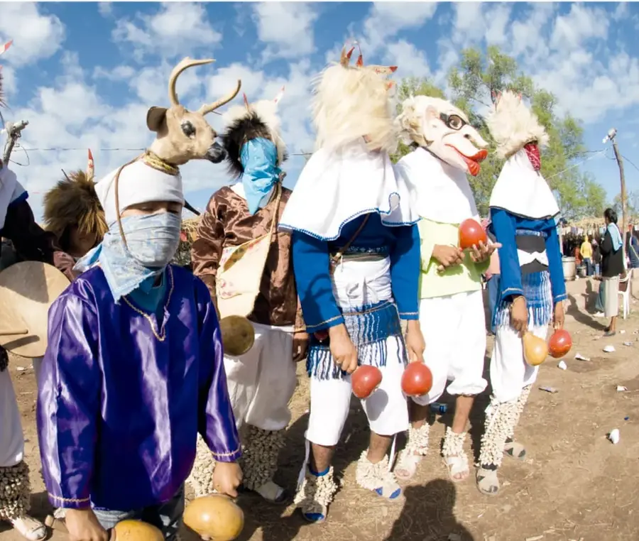 Grupo de pascolas con máscaras de animales (venado, coyote y otros), pañoletas azules, manta blanca, sonajas de calabaza rojas y tenaboim en los tobillos, durante la danza a cielo abierto.