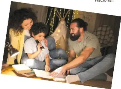 Fotografía de una familia (madre, padre e hijo) sentada junto a un árbol de navidad leyendo un libro juntos.