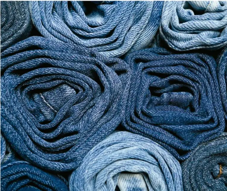 Fotografía en la que se ven varias piezas de tela de mezclilla (denim) de distintos tonos de azul enrolladas en forma de rollos, ilustrando los textiles teñidos con índigo descritos en el texto.