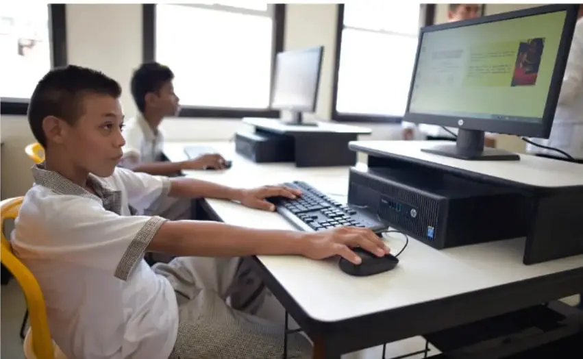 Fotografía de estudiantes de secundaria trabajando en computadoras de un aula de informática, capturando datos para su proyecto.