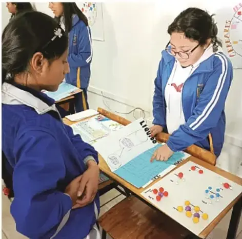 Fotografía de estudiantes de Telesecundaria con uniforme azul preparando materiales de proyectos sobre una mesa: cuadernos, fichas de colores y carpetas. Crédito fotográfico: Luis Eduardo García Medel, Tlaxcala.