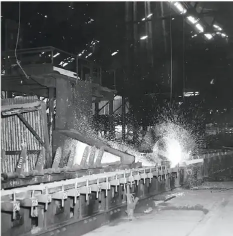 Fotografía en blanco y negro de una fábrica o taller industrial con maquinaria y chispas, que ilustra el auge industrial de la época.